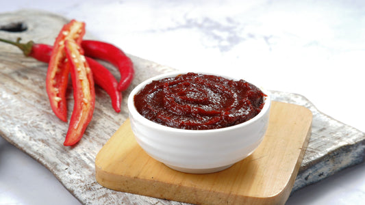 Features an arrangement of a bowl of fermented condiments on a small cutting board next to sliced hot peppers.